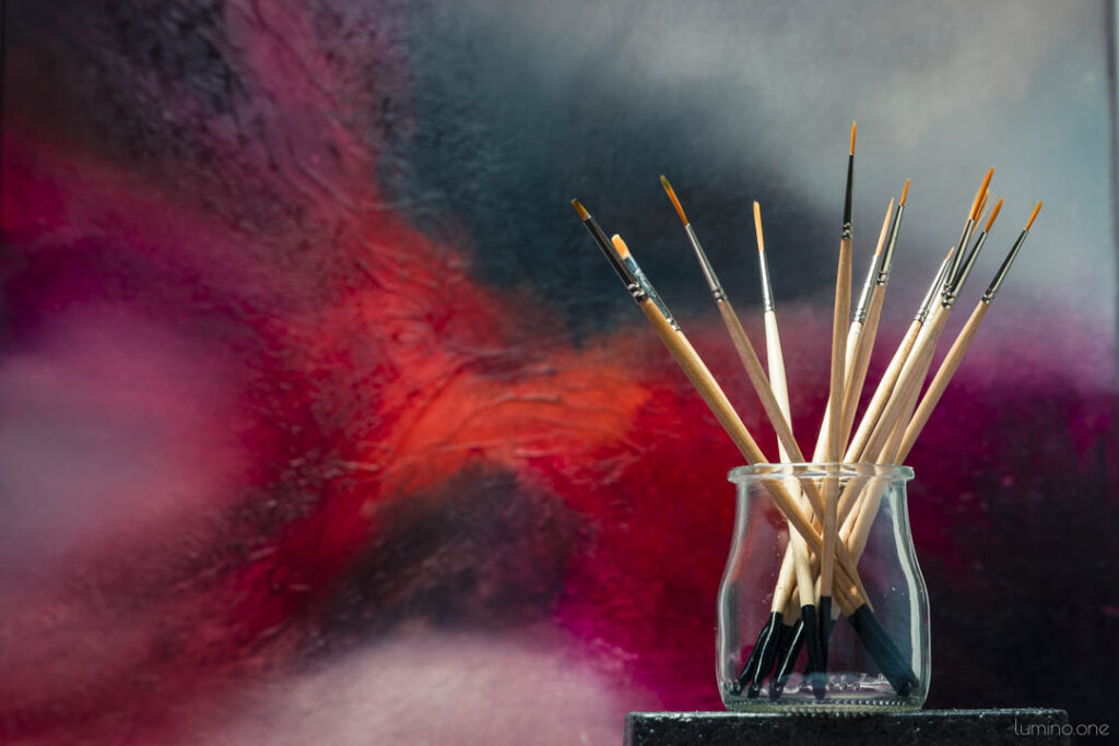 A glass jar with artist brushes with red abstract art in the background