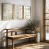 Set of three framed botanical prints featuring delicate wildflowers and dried grasses in soft neutral tones, displayed above a modern wooden bench in a bright entryway with natural light streaming through windows and potted plants