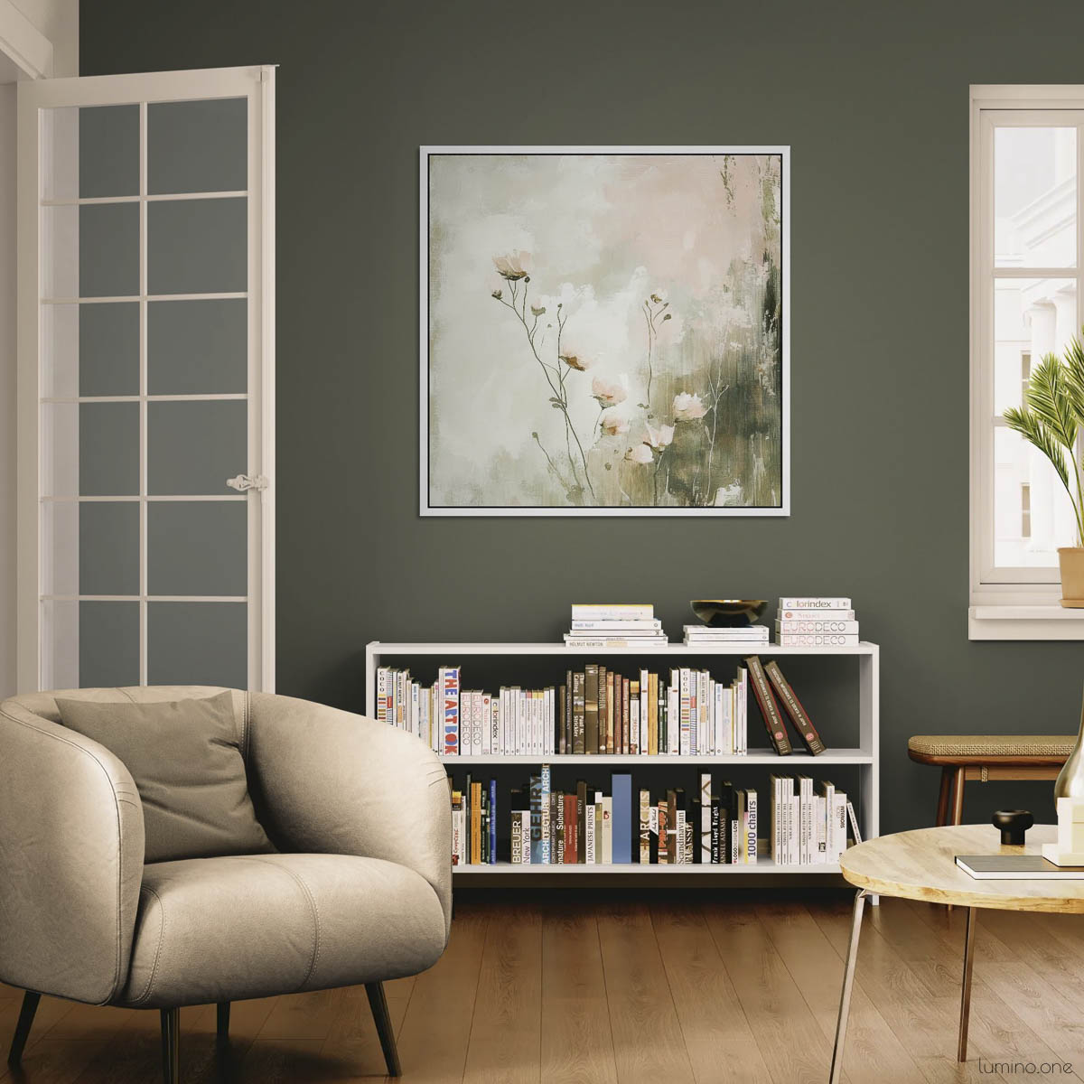 Large botanical canvas print featuring sage green wildflowers in white float frame, displayed above white bookshelf in modern living room with beige armchair, hardwood floors, and sage green accent wall