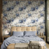 Vintage blue peony toile wallpaper as bedroom accent wall behind upholstered headboard with blue bedding and warm wood furniture