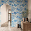 Blue Toile Peel and Stick Wallpaper - French Country Botanical P Blue and white toile peel and stick wallpaper on an entryway accent wall in a Mediterranean-style home, featuring a vintage botanical garden pattern with flowers and trees. Styled with a rustic reclaimed wood console, stacked vintage books, terracotta vases with olive branches, and marble tile floors framed by a white arched doorway.