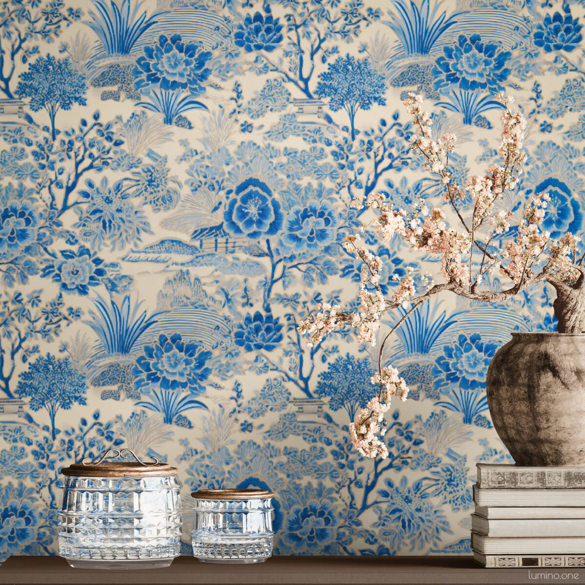 Blue Toile Peel and Stick Wallpaper - Vintage Botanical Garden P Blue and white toile peel and stick wallpaper on a full wall behind a taupe modern sideboard, featuring a vintage botanical garden pattern with large peony flowers and trees. Styled with a rustic stoneware vase holding cherry blossom branches, stacked vintage books, and crystal glass jars with brass lids.