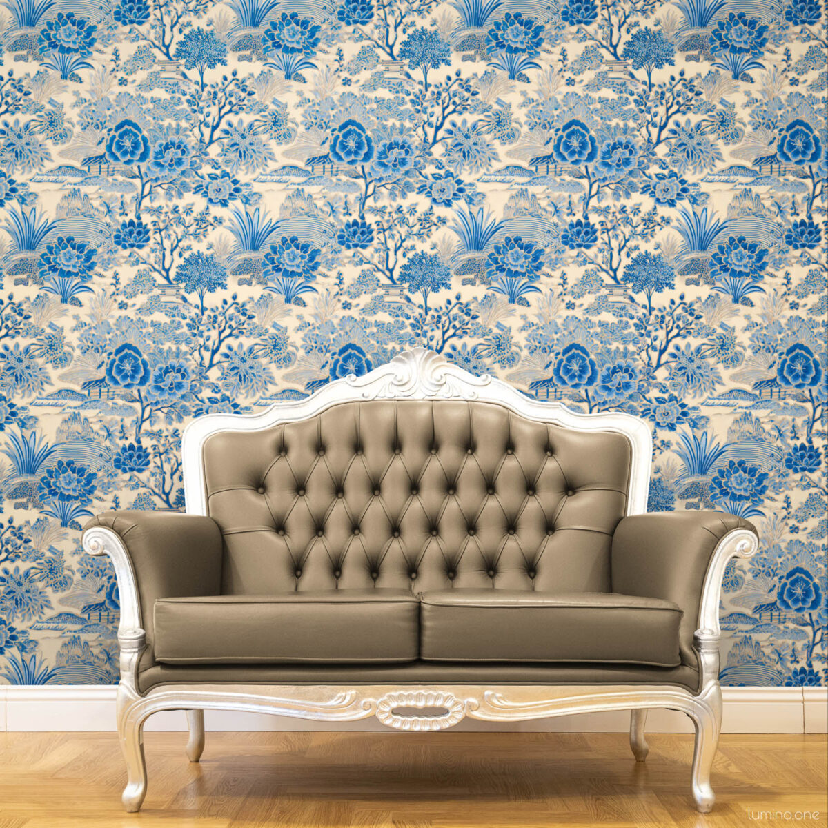 Blue and White Toile Peel and Stick Wallpaper - Vintage Botanica Blue and white toile peel and stick wallpaper covering a full wall behind an ornate French-style tufted leather loveseat with silver carved wood frame, featuring a vintage botanical garden pattern with large peony flowers and trees. Styled on a warm honey herringbone wood floor, showcasing a classic French country living room aesthetic.