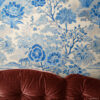 Blue and White Toile Wallpaper - French Country Botanical Garden Blue and white toile wallpaper featuring a classic botanical garden scene with flowers and trees, styled behind a tufted burgundy velvet sofa. French country vintage toile design available as peel and stick removable wallpaper.